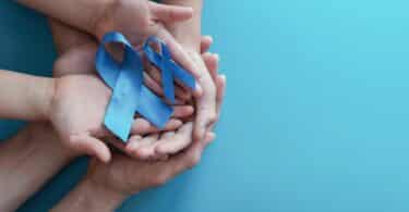 Imagem das mãos de um adulto e de uma criança segurando dois laços de fita na cor azul, simbolizando o Setembro Azul, que é um mês de conscientização e visibilidade para a comunidade surda, dedicado à celebração das suas conquistas e à divulgação da cultura surda e da Libras (Língua Brasileira de Sinais).