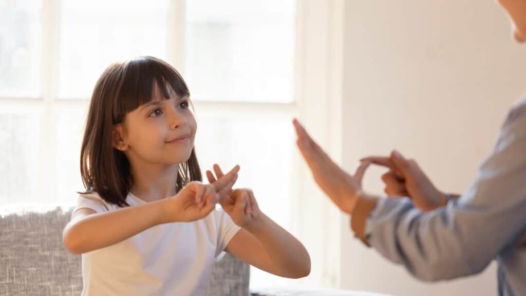 Mãe e filha sentadas no sofá se comunicando de forma não verbal com a linguagem de sinais.