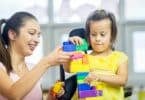 Imagem de uma mãe atípica, brincando com sua filha que precisa de cuidados especiais. Elas estão montando uma peça com jogo de Lego.