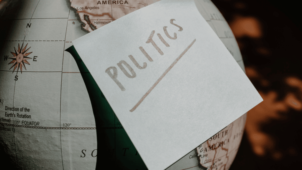 Nota adesiva com a palavra “POLITICS” escrita em letras maiúsculas colocada sobre um globo terrestre, parcialmente mostrando a América do Norte e a América do Sul.