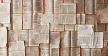 Vários livros antigos abertos lado a lado, formando um fundo preenchido por páginas de texto amareladas.