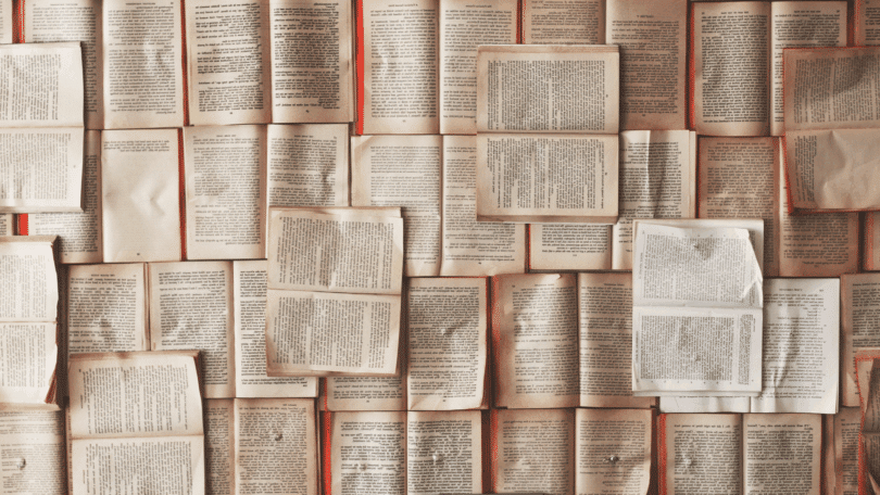 Vários livros antigos abertos lado a lado, formando um fundo preenchido por páginas de texto amareladas.