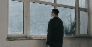 Um homem está em pé e observa através de uma grande janela.