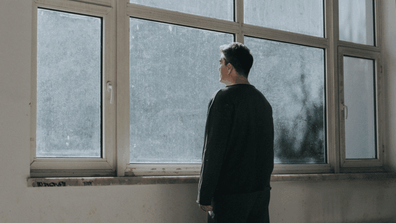 Um homem está em pé e observa através de uma grande janela.