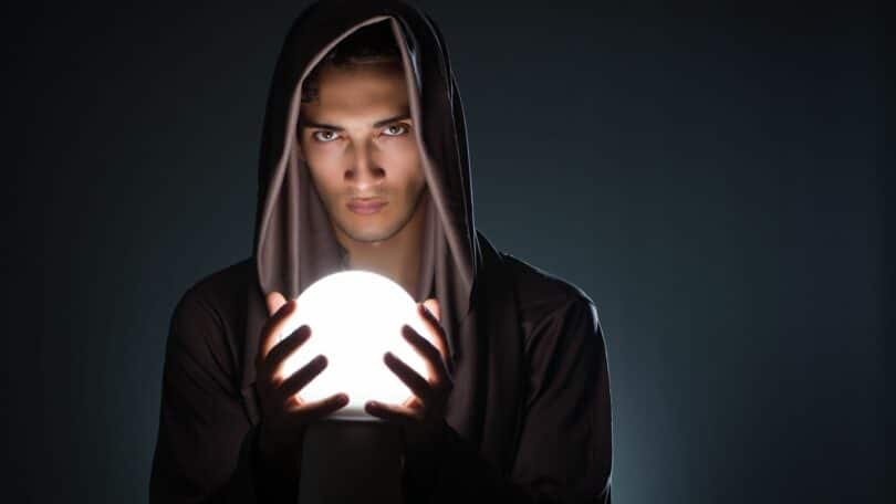 Imagem de um homem, usando uma túnica marrom, segurando uma bola de cristal, trazendo o conceito de jovem místico e espiritualidade.