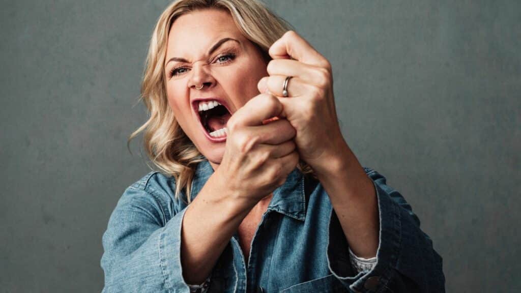 Imagem de uma mulher com um semblante simbolizando uma raiva ou mesmo uma vingança. Ela mexe com as mãos e parece que está gritando.
