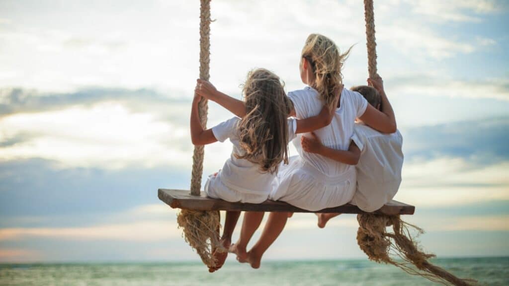 Imagem de uma mãe e seus dois filhos sentandos em um balanço ao ar livre, simbolizando o conceito de uma relação verdadeira.