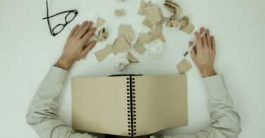 Imagem de uma pessoa debruçada sobre uma mesa, com o óculos de grau deixado ao lado, além de vários papéis picados. A foto simboliza uma pessoa com os sintomas do Transtorno da Sobrecarga Sensorial.