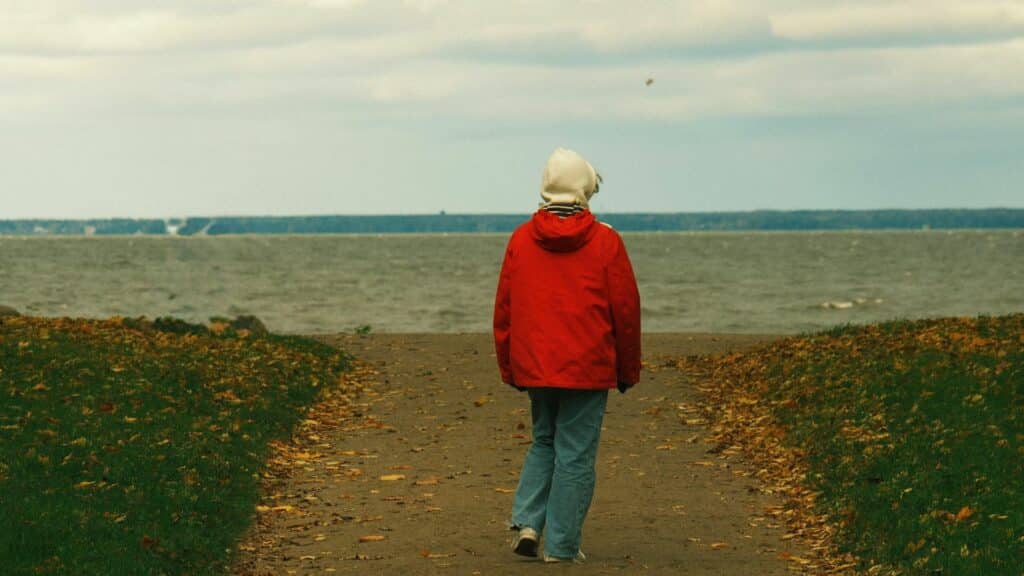 Imagem de uma pessoa usando um casaco de frio na cor vermelha. Ela possui o ranstorno da Sobrecarga Sensorial - TSS e está caminhando em direção ao mar.