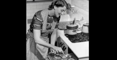 Imagem de uma dona de casa sorridente mexendo algumas costeletas no seu forno.