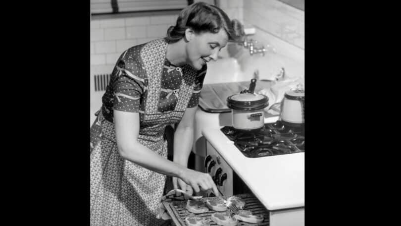 Imagem de uma dona de casa sorridente mexendo algumas costeletas no seu forno.