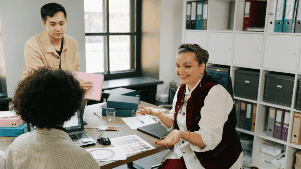 Um grupo de três funcionários de uma empresa estão discutindo sobre os negócios ao redor de uma grande mesa.