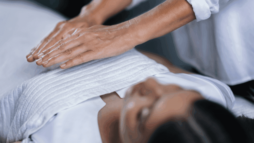 As mãos de um profissional fazendo reiki em uma cliente estão em destaque na imagem.