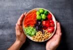 Imagem das mãos de um homem segurando um prato com legumes e vegetais, simbolizando o conceito do vegetarianismo.