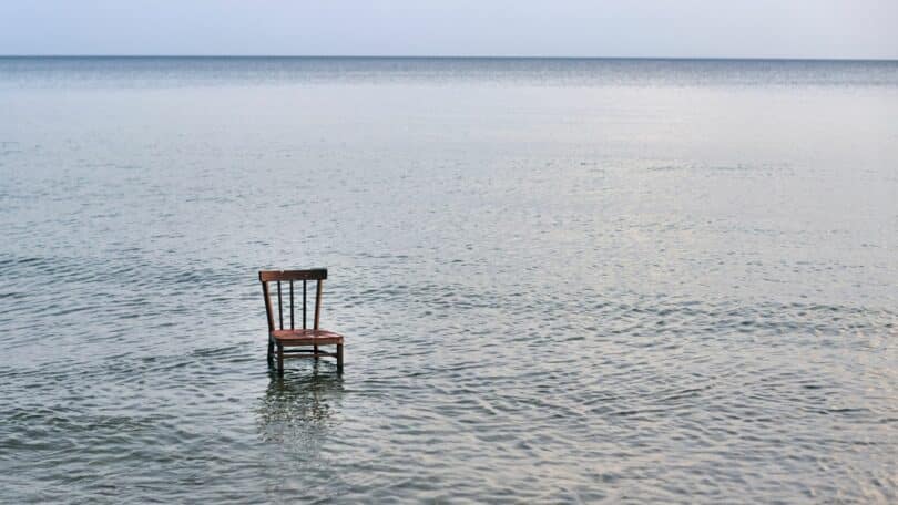 Imagem do mar e em destaque uma cadeira de madeira vazia, simbolizando o conceito do cansaço existencial que surge quando a vida perde sentido e passamos a viver no automático.