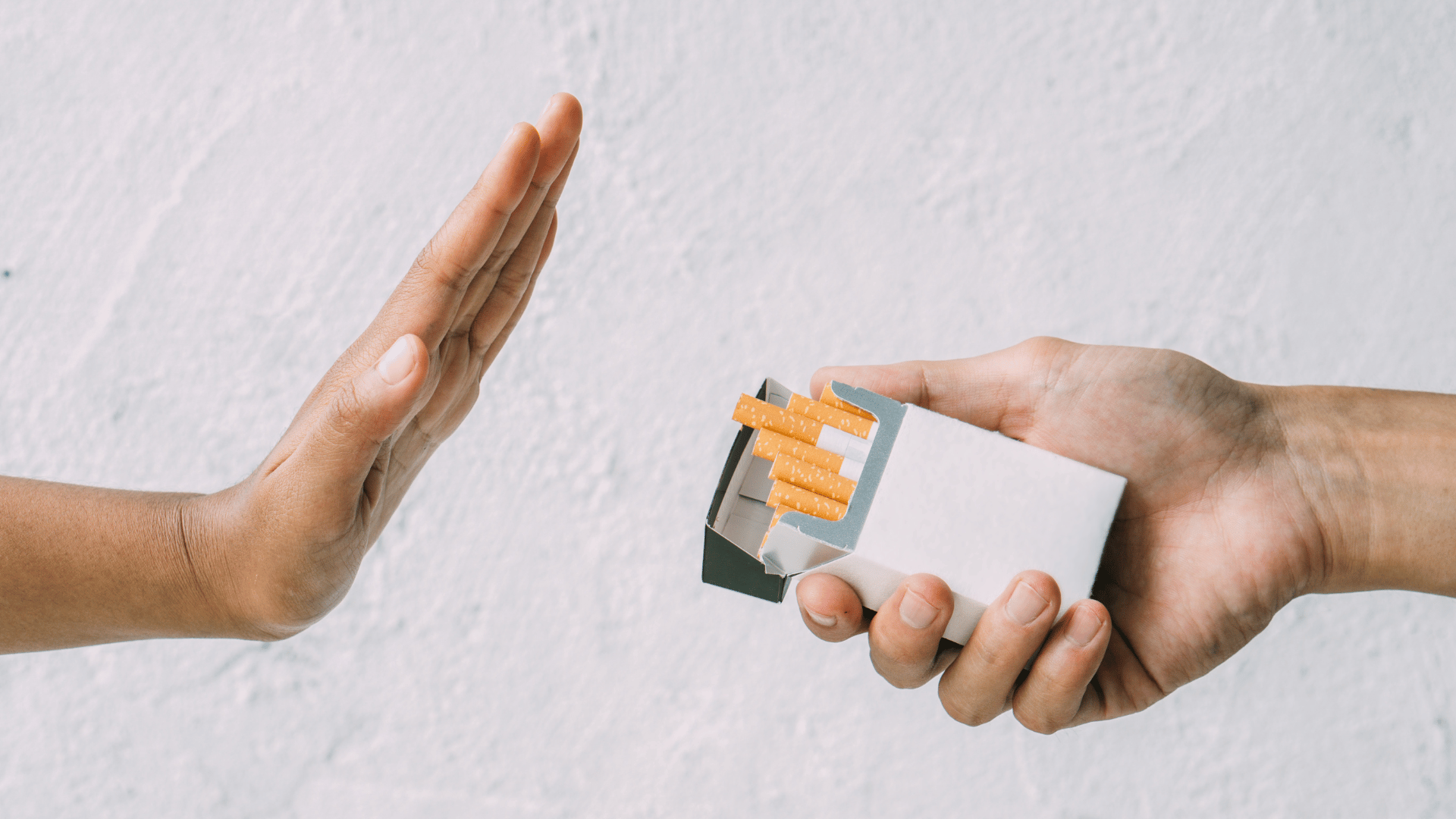 Mão aberta em gesto de recusa diante de outra mão oferecendo um maço de cigarros.