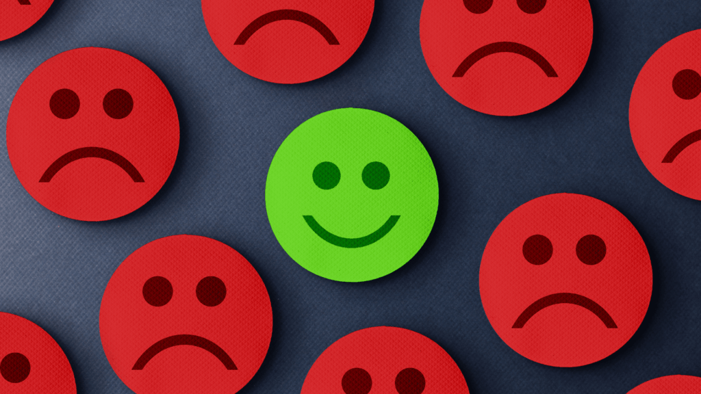 Ilustrações de alguns rostos com emoções negativas na cor vermelha. E a ilustração expressando emoção positiva na cor verde está no centro da imagem.