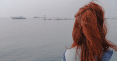Uma mulher jovem e ruiva está observando o mar.