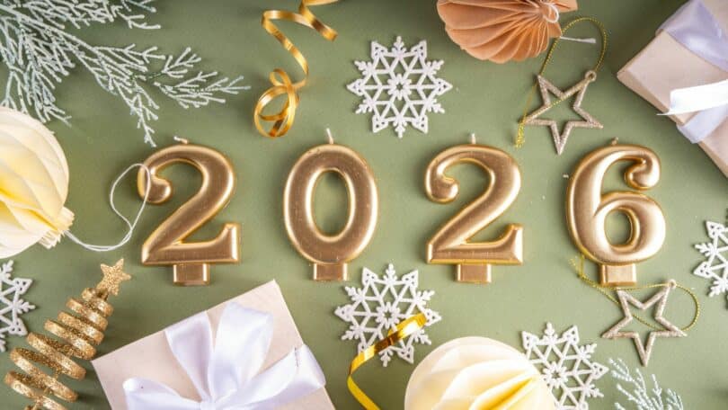 Imagem de 4 velas de aniversário, representando o ano de 2026. Ao fundo, vários elementos que simbolizam as festas de fim de ano.