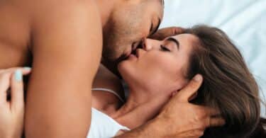Imagem de um casal deitado se beijando. Ele está sobre ela.