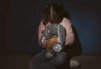 Imagem de uma menina assustada segurando um brinquedo, encostada perto de uma parede azul. A foto traz o conceito de Violência contra as crianças.