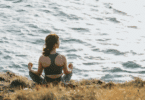 Uma mulher jovem está meditando à beira do mar.