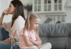 Uma mãe e uma filha criança estão de costas uma para a outra e sentadas em um sofá. A menina está chateada e a mãe está ignorando-a.