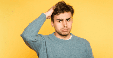 Um homem jovem está com uma mão na cabeça, aparentando estar confuso.