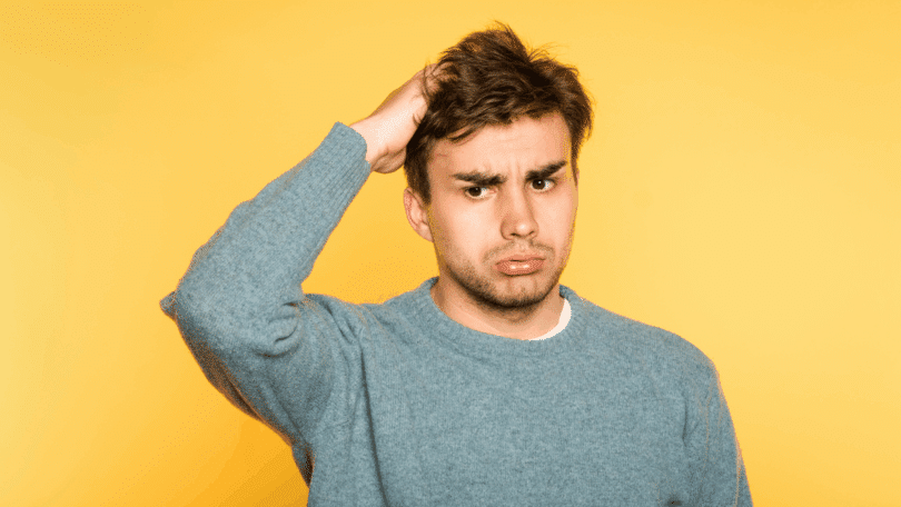 Um homem jovem está com uma mão na cabeça, aparentando estar confuso.