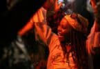 Imagem de uma mulher angolana, feliz e dançando ao som de uma música ao vivo, em uma área com várias pessoas.