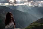 Imagem de uma mulher de cabelos longos e óculos de sol, sentada olhando para uma vista tranquila para a montanha nos Alpes Suíços.