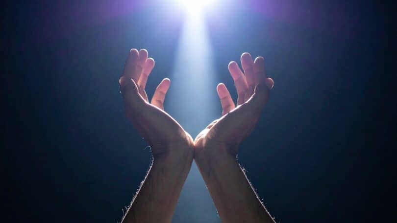 Imagem de um feixe de luz e das mãos de um homem postas sobre ela, trazendo o conceito de conexão com Deus e liberdade espiritual.