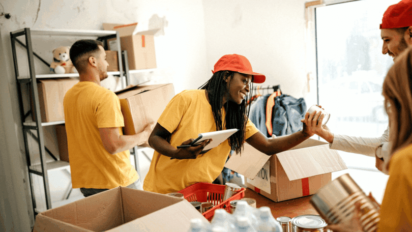 Voluntários organizando doações e alimentos enlatados em caixas dentro de um espaço comunitário.