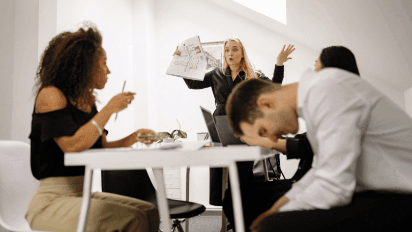 Mulher apresentando um projeto em reunião enquanto colegas parecem cansados ou desmotivados.