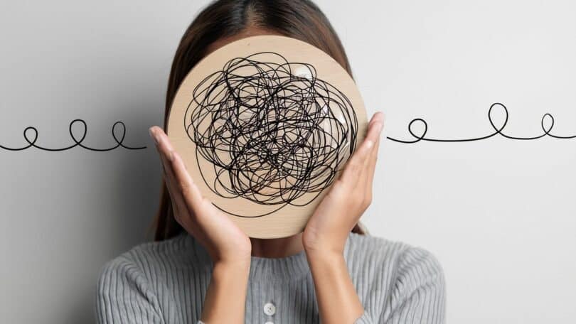 Imagem de uma mulher com o rosto coberto com um círculo cheio de fios que representam a saúde mental em torno do trabalho.