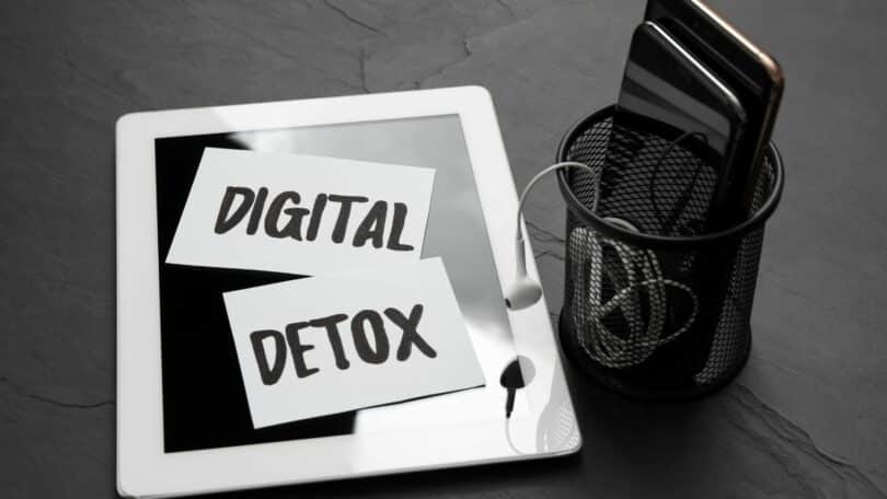 Imagem em preto e branco de uma tela de Ipad e um celular em uma cesto preto. Na tela está escrito a frase: DIGITAL DETOX - em português: DETOX DIGITAL.