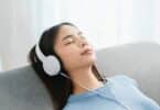 Imagem de uma mulher sentada em seu sofá, ouvindo músicas com um fone de ouvido. A foto traz o conceito de epidemia da solidão.
