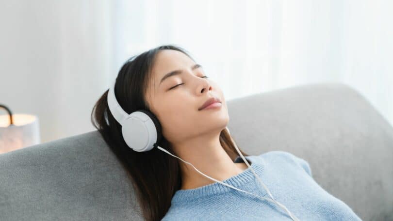 Imagem de uma mulher sentada em seu sofá, ouvindo músicas com um fone de ouvido. A foto traz o conceito de epidemia da solidão.