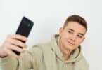 Imagem de um jovem da geração Z, usando um moletom verde claro e fazendo uma selfie com o celular.