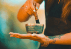 Mulher segurando um sino tibetano e usando um bastão para tocá-lo, em momento de meditação.