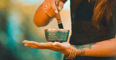 Mulher segurando um sino tibetano e usando um bastão para tocá-lo, em momento de meditação.