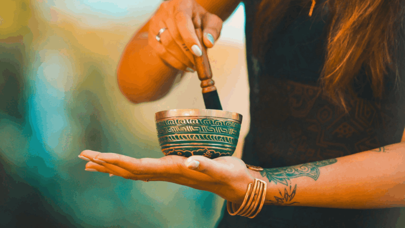 Mulher segurando um sino tibetano e usando um bastão para tocá-lo, em momento de meditação.