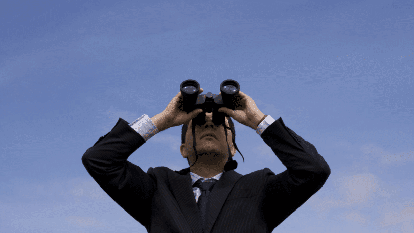 Homem de terno usando binóculos e olhando para o céu.