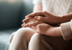 Mãos entrelaçadas em gesto de apoio e cuidado, transmitindo acolhimento e empatia.
