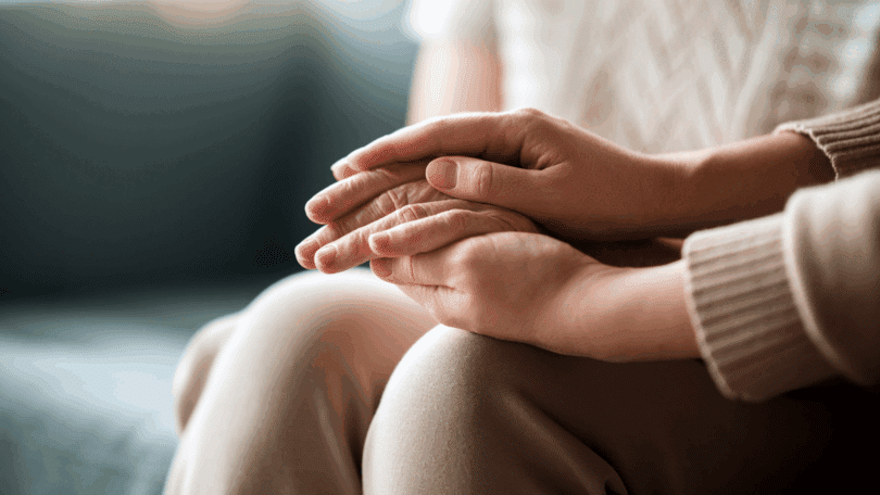 Mãos entrelaçadas em gesto de apoio e cuidado, transmitindo acolhimento e empatia.