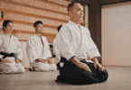 Grupo em trajes de artes marciais pratica meditação ajoelhado em um dojo.