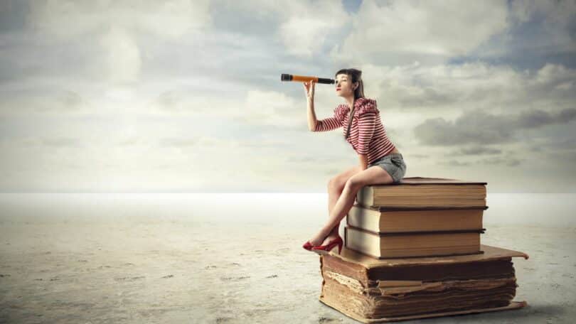 Imagem de uma mulher sentada sobre alguns livros, usando uma lupa olhando para o futuro.