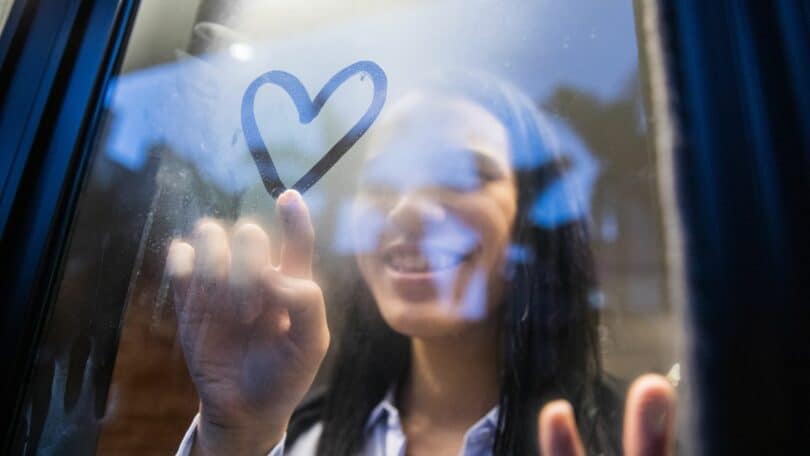 Imagem de uma mulher desenhando um coração em uma janela de vidro embaçada. A foto traz o conceito da mulher que faz de tudo e ainda não despertou e está em busca do autoconhecimento.