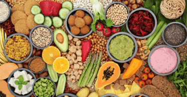 Variedade de alimentos naturais e vegetais organizados em mesa, com grãos, frutas, legumes e preparações saudáveis coloridas.