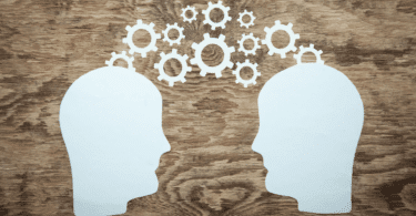 Silhuetas de duas cabeças conectadas por engrenagens simbolizam troca de ideias, comunicação e funcionamento da mente.